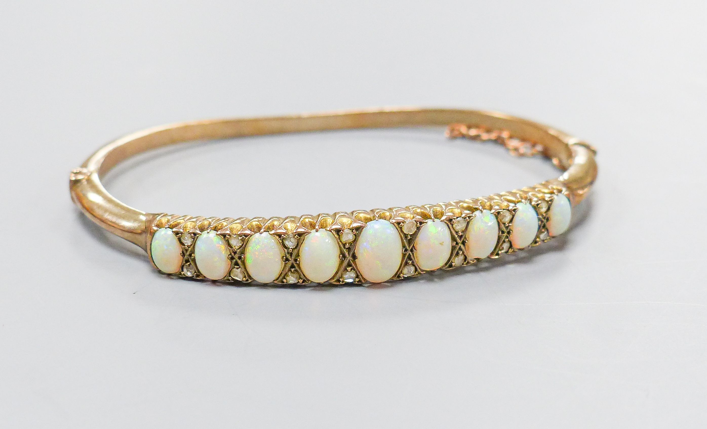 An early 20th century gold plated graduated nine stone white opal set hinged bracelet, with diamond chip spacers, in fitted box.